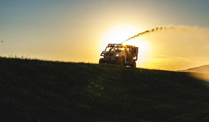 Polaris Government and Defense DAGOR military vehicle spraying water against a vibrant sunset over a grassy hill.
