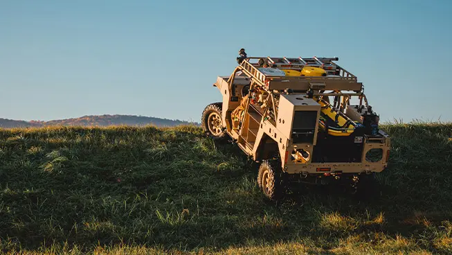 Rear view of a Polaris Government and Defense DAGOR climbing a grassy incline, showcasing its rugged design and externally mounted equipment.