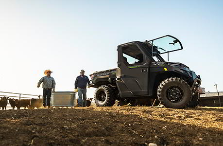 Dos personas cargando una cubeta a lado de un Polaris RANGER.