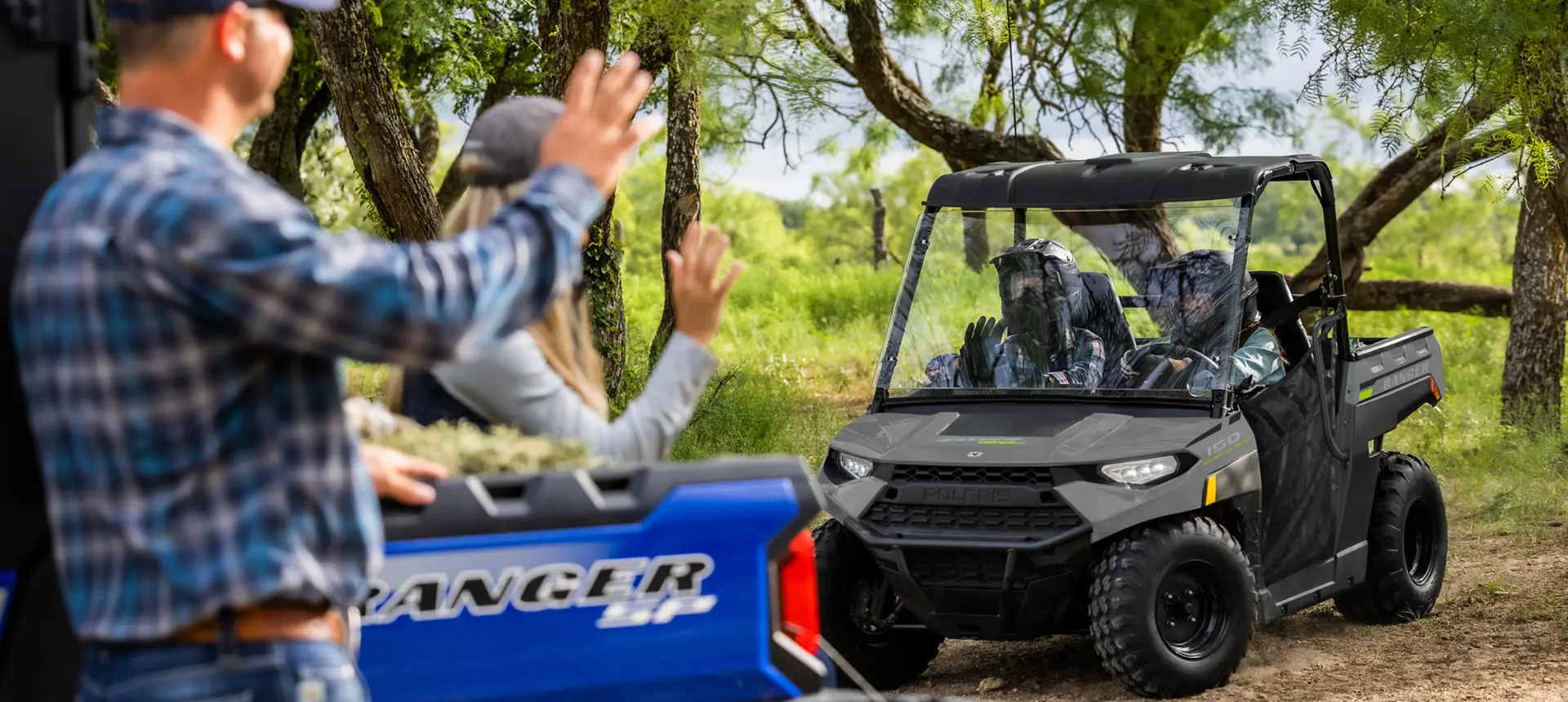 Two people inside a Ranger 150 efi vehicle greeting another couple that is nearby