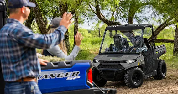 Two people inside a Ranger 150 efi vehicle greeting another couple that is nearby
