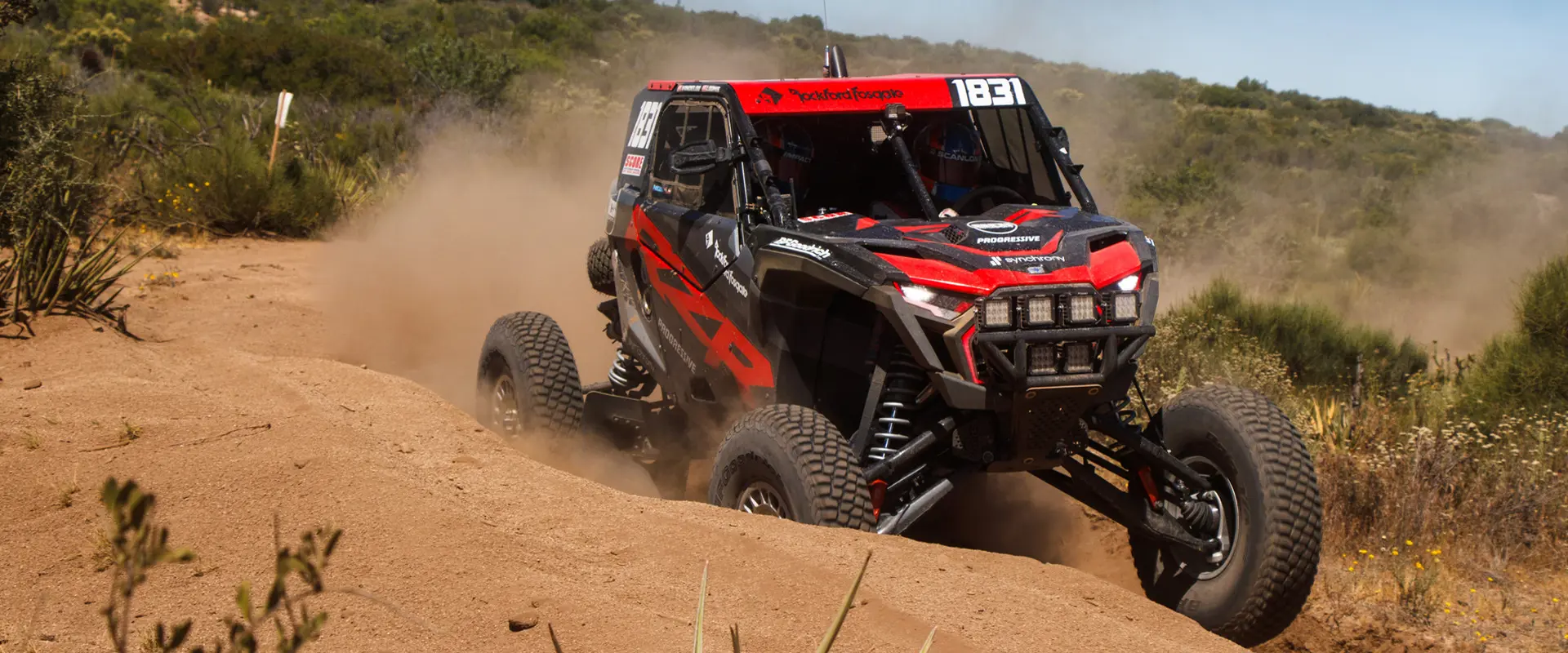 Côte à côte Polaris RZR Pro XP 2025 prenant un virage sur un sentier poussiéreux et projetant du sable.