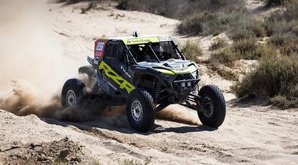 Un Polaris RZR Pro XP 2025 Side-by-Side corriendo en un sendero polvoriento, levantando arena en una toma de acción dinámica.