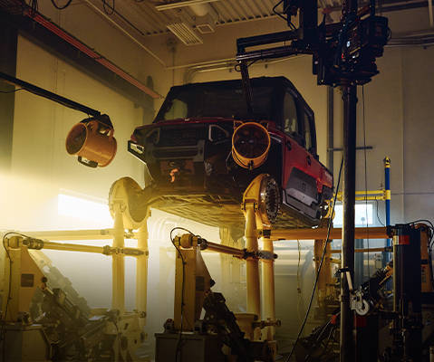 A Polaris RANGER vehicle is elevated off the ground, with its front end facing downwards at an angle, suggesting an impact test. It is supported by a metal rig with various equipment around it, including lighting and sensors, to monitor the test parameters.