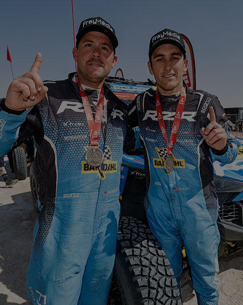 Brock Heger and Max Eddy Jr posing in front of a RZR Pro R Factory side-by-side wearing their first place medals.