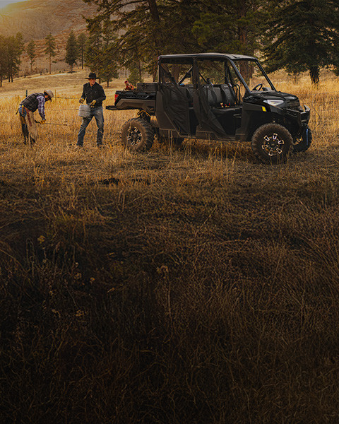 A black Polaris RANGER Crew XP 1000 Texas Edition is parked in a dry, grassy field while two ranchers work nearby with fencing.