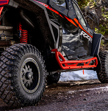 A Polaris RZR SxS with Pro Armor Crawler XP tires is stopped on a muddy road.