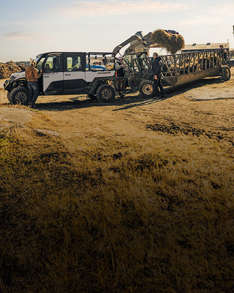 White Polaris RANGER CREW XD 1500 Extreme Duty UTV on a farm, with people and a skid steer loading hay into a feeder.
