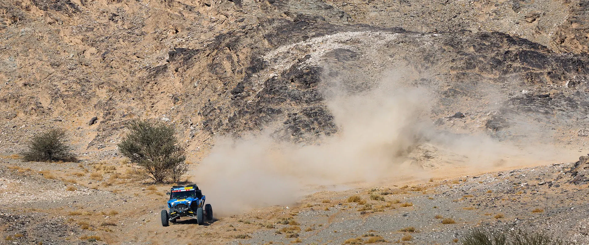 Dakar Rally RZR Pro R Factory driving up hill kicking up dust cloud.