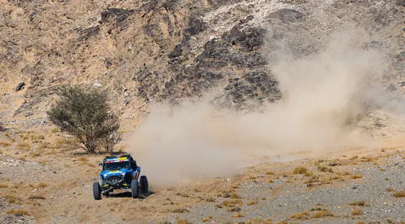 Dakar Rally RZR Pro R Factory driving up hill kicking up dust cloud.