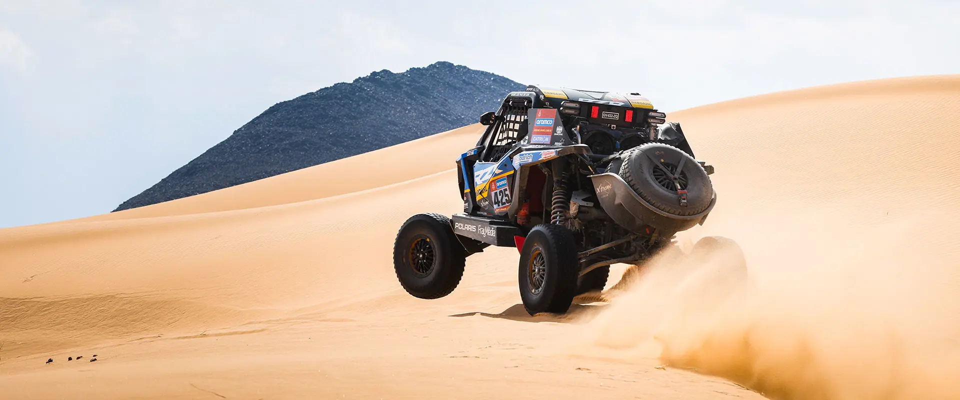 A RZR Pro R Factory jumps a large sand dune with dust cloud at the Dakar Rally.