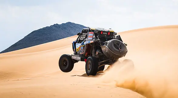 A RZR Pro R Factory jumps a large sand dune with dust cloud at the Dakar Rally.