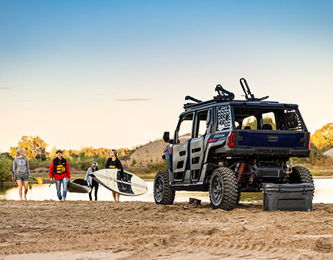 Four people standing and sitting on two Sportsman ATVs in an outdoor setting with a forested background.