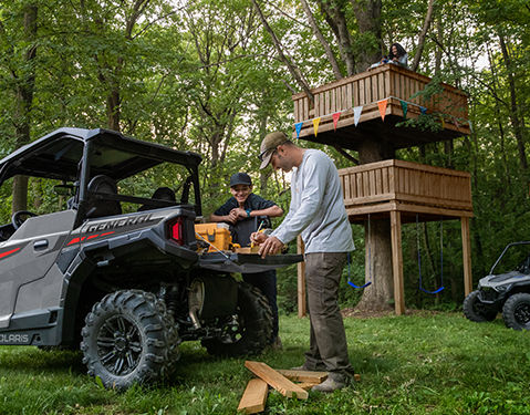 A person riding a Polaris Sportsman ATV on a rocky and dusty trail in a mountainous area, wearing protective gear including a helmet.