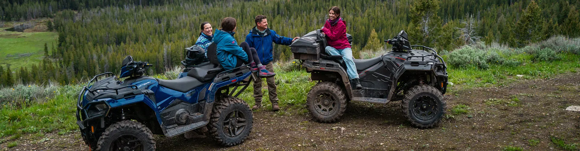 A blue Polaris RANGER SP 570 UTV parked on a dirt path in a lush, green outdoor setting with three people standing nearby under the shade of trees.