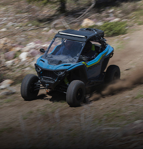 A blue RZR Trail S SxS kicks up dust on a rocky trail.
