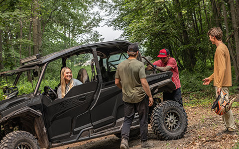 A woman smiling from the driver's seat of a black Polaris GENERAL XP 1000 SxS/UTV while 3 men grab gear from the cargo box.