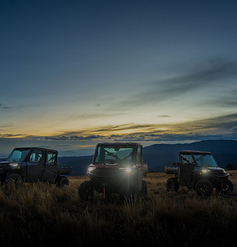 Polaris RANGER UTVs parked in a field with mountains at sunset.