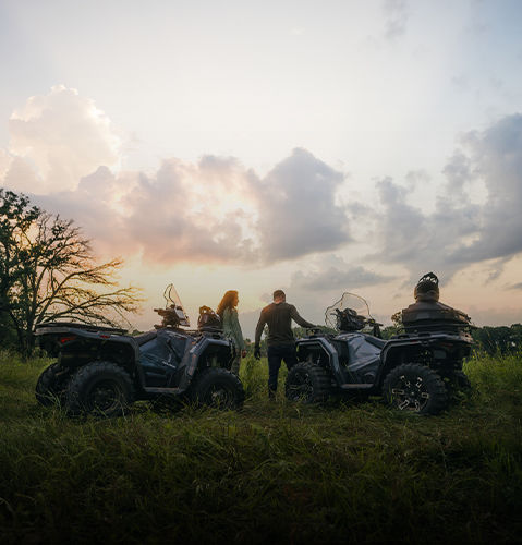 Una pareja con ATV Polaris Sportsman disfrutando el atardecer en un campo.