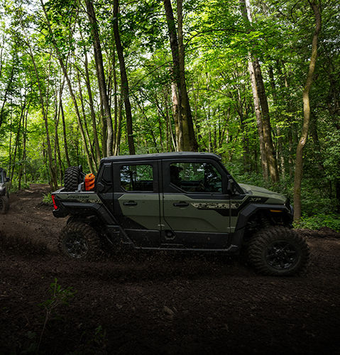 Dos Side-by-Side Polaris XPEDITION XP verdes de cinco asientos en un sendero lodoso a través de un bosque denso.
