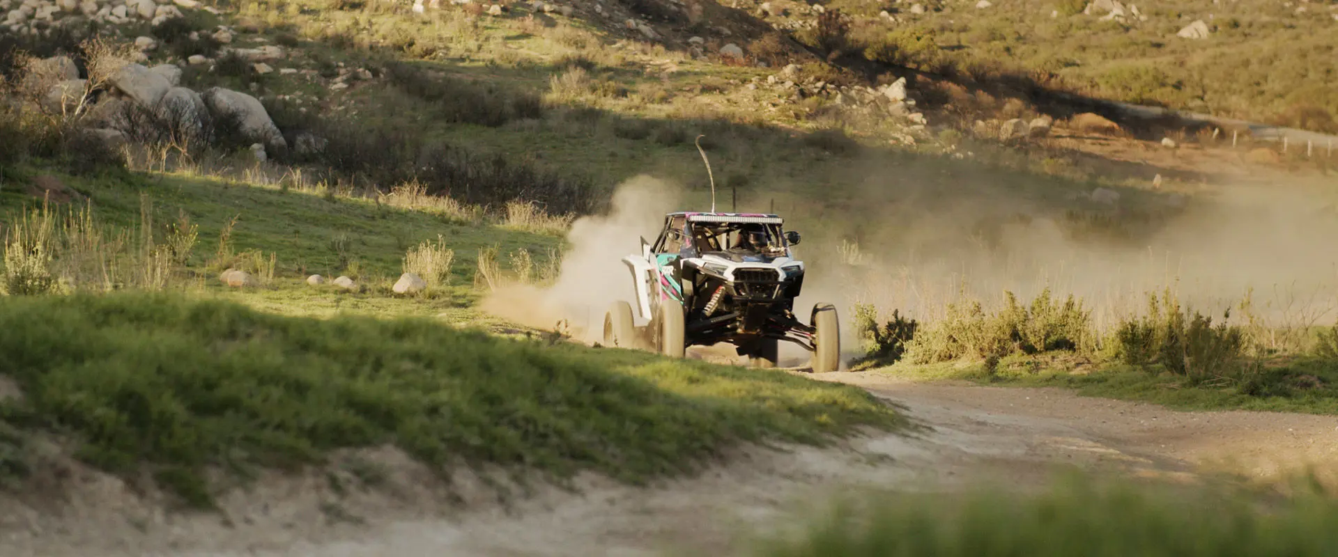 Fernanda Montiel racing her Polaris RZR SxS on a dusty dirt track, kicking up dirt in a rural landscape.
