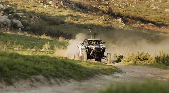Fernanda Montiel racing her Polaris RZR SxS on a dusty dirt track, kicking up dirt in a rural landscape.