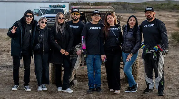 Fernanda Montiel and her friends posing in front of a Polaris RZR SxS at a racing event.