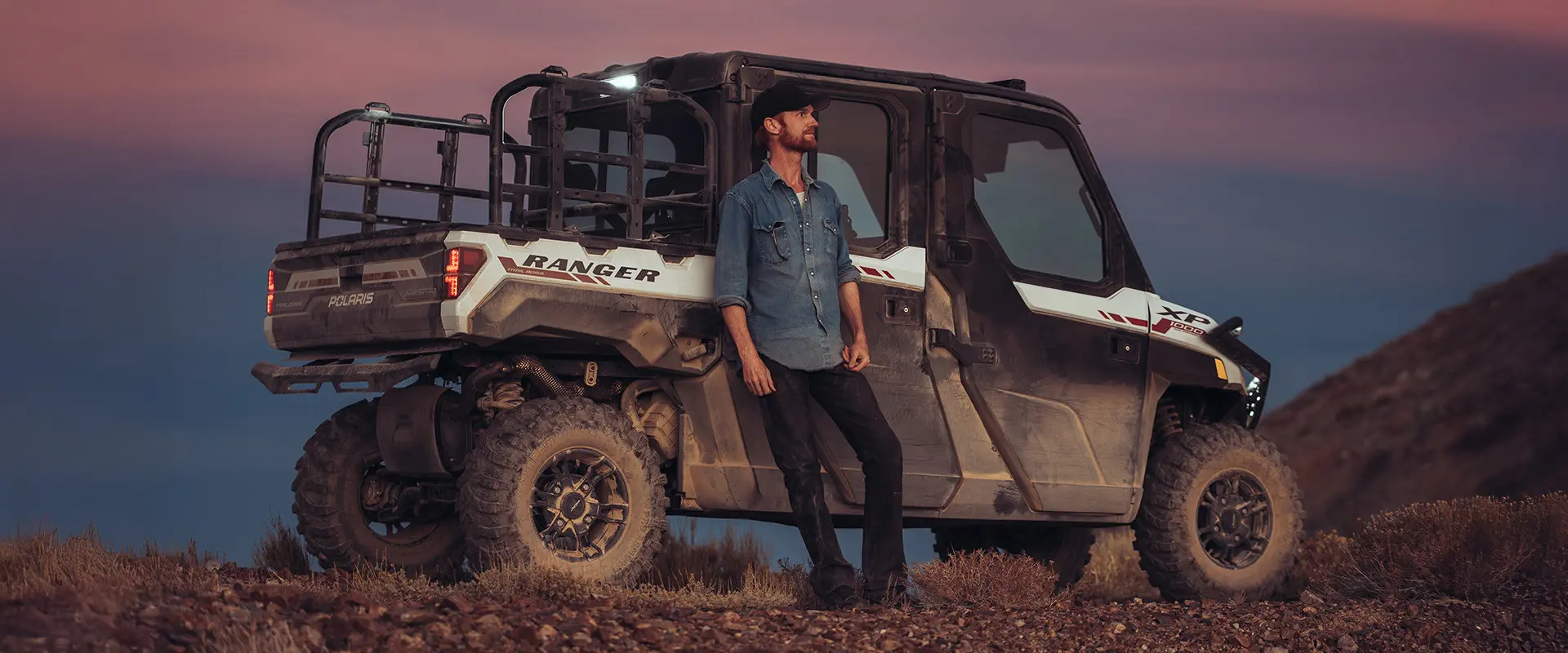 Brent Underwood leans against a Polaris RANGER XP 1000 during sunset in a rocky, arid environment.
