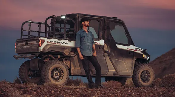 Brent Underwood leans against a Polaris RANGER XP 1000 during sunset in a rocky, arid environment.