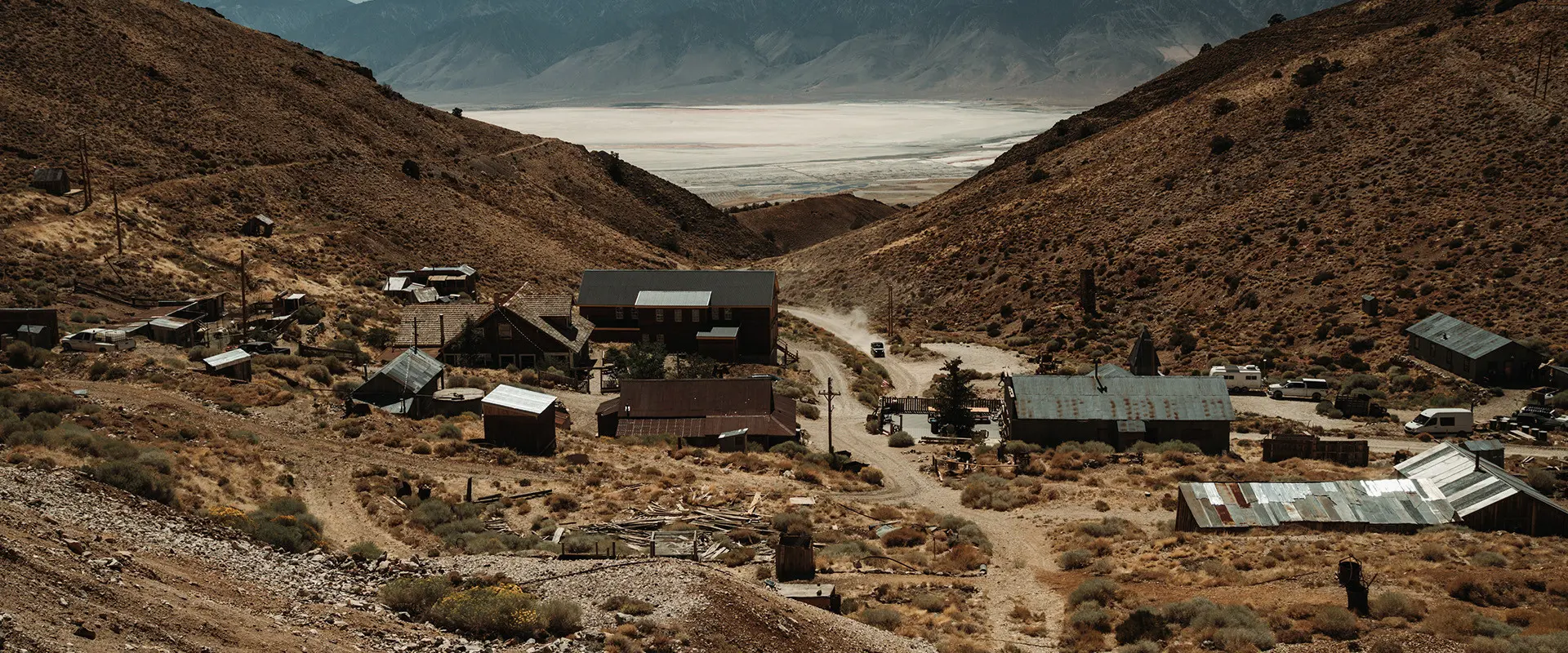 Aerial view of a remote, old mining town nestled in a dry valley with a vast dry lakebed and mountains in the background.