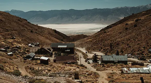 Aerial view of a remote, old mining town nestled in a dry valley with a vast dry lakebed and mountains in the background.