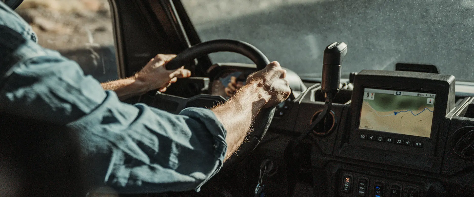 Close-up of hands on the steering wheel of a Polaris RANGER XP 1000, showing a display of a RIDE COMMAND map.