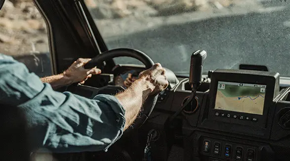 Close-up of hands on the steering wheel of a Polaris RANGER XP 1000, showing a display of a RIDE COMMAND map.