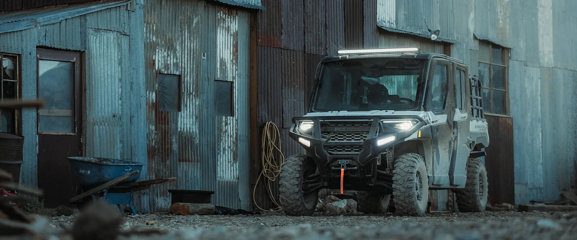 A Polaris RANGER XP 1000 UTV is parked next to an old corrugated metal building with a wheelbarrow nearby.