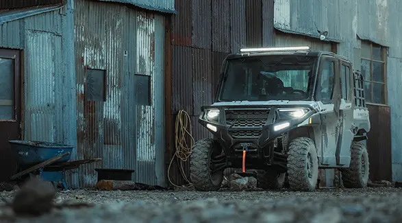 A Polaris RANGER XP 1000 UTV is parked next to an old corrugated metal building with a wheelbarrow nearby.