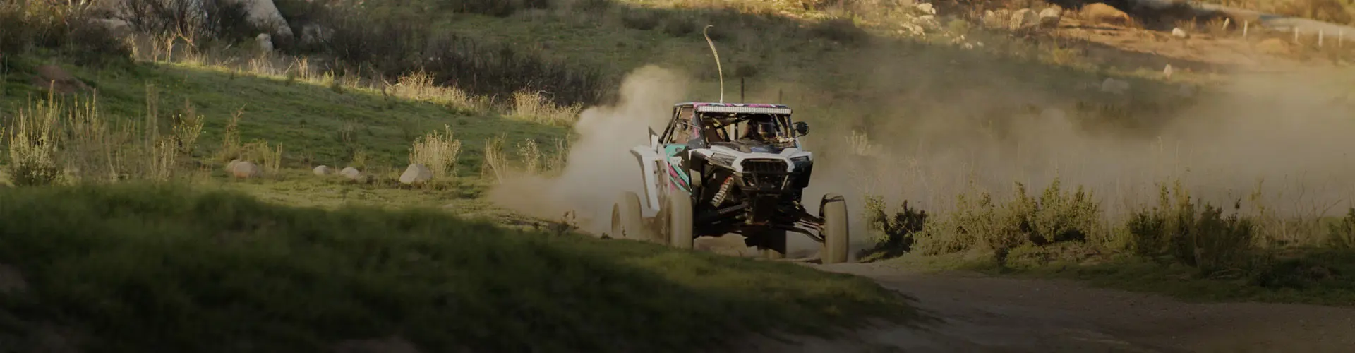 Fernanda Montiel racing her Polaris RZR SxS on a dusty dirt track, kicking up dirt in a rural landscape.