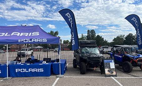Polaris RANGER UTV and Polaris RZR Side-by-Side displayed beside a Polaris-branded tent with flags, tables, and promotional signage at an outdoor event venue.