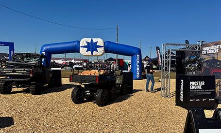 Outdoor Polaris event display with a RANGER CREW and a 6-wheeled RANGER under a blue inflatable arch, alongside a ProStar engine exhibit.