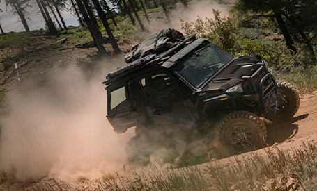 A black Polaris XPEDITION side-by-side vehicle kicks up a large cloud of dust while speeding along a forest trail.