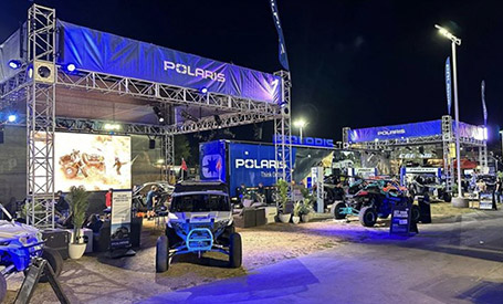 Night shot of a Polaris event with blue lights, metal trusses, a large video screen, and various Polaris vehicles.