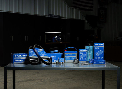 Polaris Pro Series service and maintenance parts displayed on a workshop table, including drive belts, air filters, brake pads, batteries, bearings, and drivetrain components.