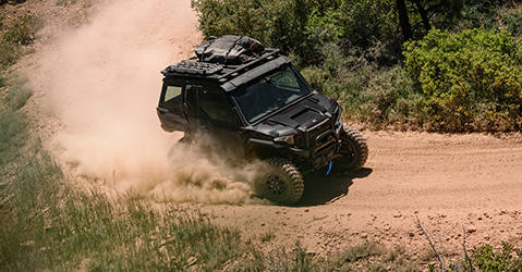 Polaris Off-Road UTV vehicle equipped with Rhino-Rack® Storage accessories aggressively traversing a dirt curve and leaving dust behind.