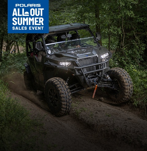 Polaris RANGER UTV driving through a dense forest trail, navigating muddy terrain with headlights on and tall greenery surrounding the narrow path.
