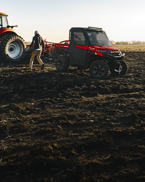 Red Polaris RANGER XP 1000 UTV parked beside a tractor and farm equipment in a freshly plowed field.