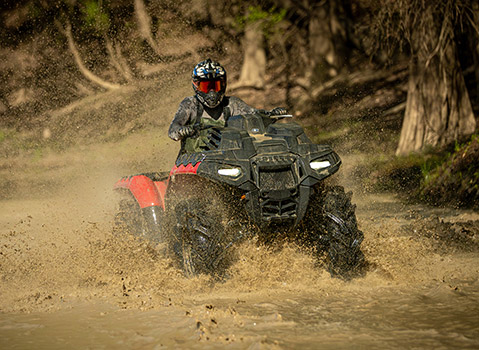 Polaris Sportsman ATV rider splashing through a muddy trail, showcasing off-road performance and recreational trail riding capabilities.