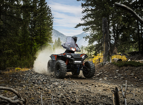 Polaris Sportsman ATV riding along a rocky forest trail, kicking up dust while navigating rugged mountain terrain.