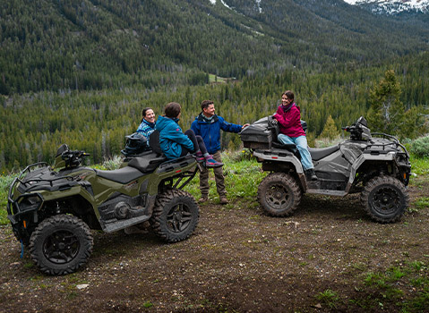 Two Polaris Sportsman Touring ATV models parked at a scenic mountain overlook, with riders gathered beside the vehicles above a forested valley.