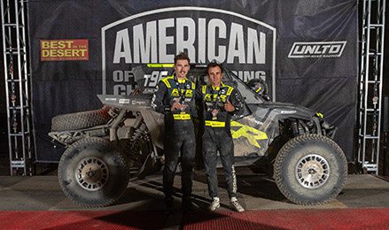 Brock Heger and Ethan Groom pose with a mud-covered Polaris RZR Pro R Factory vehicle at the Vegas to Reno racing event.