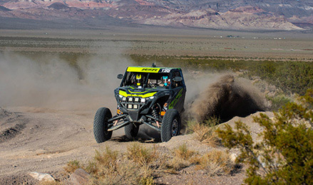 Polaris RZR Pro R Factory SxS powers through a rugged desert course, kicking up dust and dirt against a mountain backdrop.