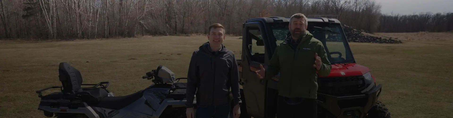 Pat McArdle and Matt standing outdoors beside a Polaris Sportsman Touring ATV and a Polaris RANGER XP 1000 UTV in an open field.